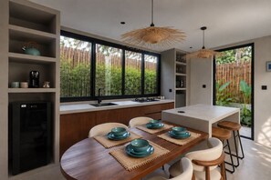 A modern kitchen with a dining area, large windows, and a view of greenery. - Alma Villas (San Juan)