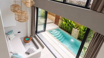 Un interno moderno con piscina, ampie finestre e una zona relax con cuscini.