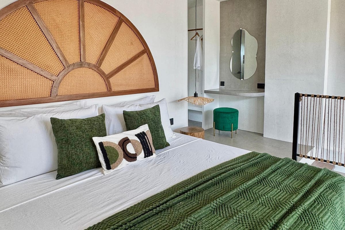 A modern bedroom with a large bed, a wooden ceiling fan, a round woven headboard, and a green throw blanket.