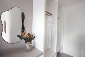 A bathroom with a round mirror, a vase with dried flowers, and a white robe hanging on a rack. - Alma Villas (San Juan)