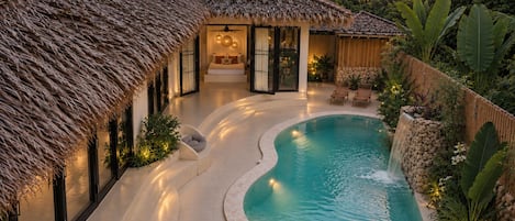 Una piscina de borde curvo, una estructura de techo de paja y una cascada.