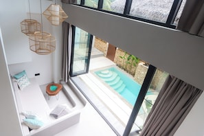 A modern room with a large window, a built-in seating area, and a view of a swimming pool. - Alma Villas (San Juan)