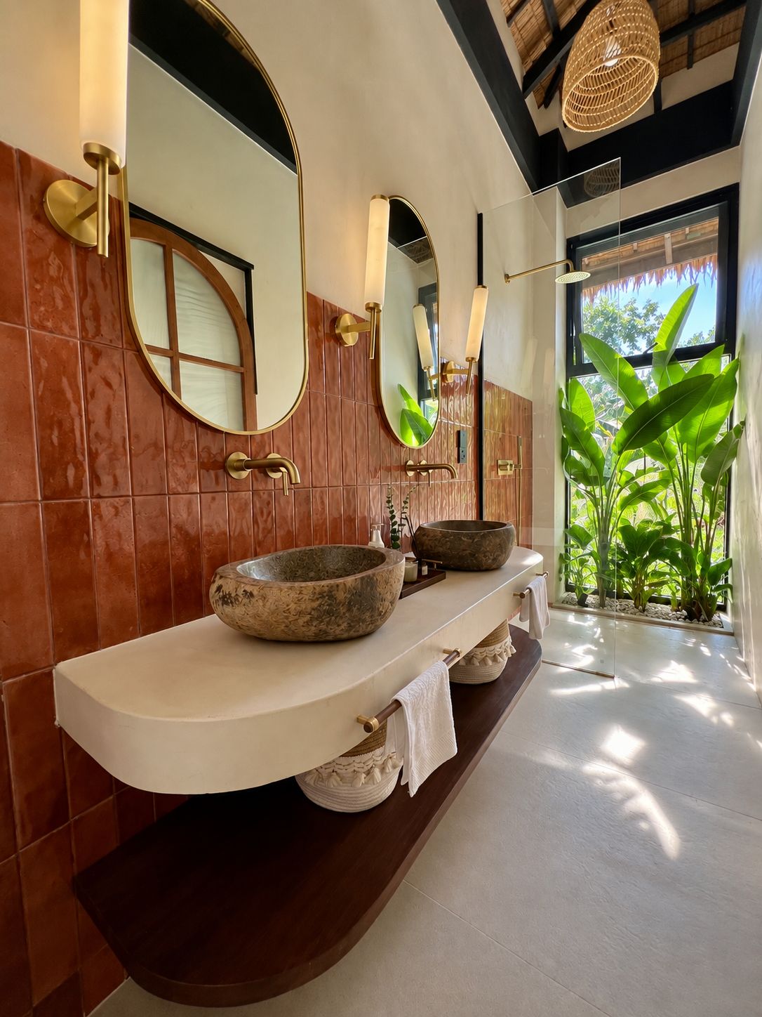 A bathroom with a large mirror, two stone basins, and a view of greenery outside.