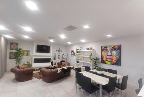 Un salon moderne comprenant un canapé, une table à manger et des chaises, un téléviseur fixé au mur et un tableau aux couleurs vives.