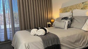 Een hotelkamer met een bed, gordijnen, een lamp en uitzicht.