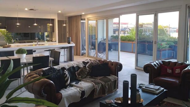Een moderne woonkamer met een bank, een salontafel en een eethoek, met een keuken op de achtergrond.