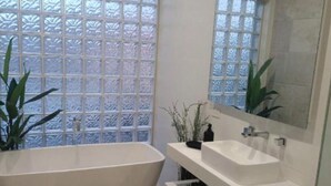 Een moderne badkamer met een vrijstaand bad, een grote spiegel en een raam met geëtst glas.