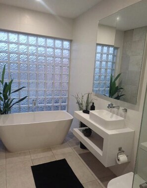 A modern bathroom with a freestanding bathtub, a large mirror, and a window with frosted glass. - Luxury 2br CBD View Apartment with spectacular balcony! (Kent Town)