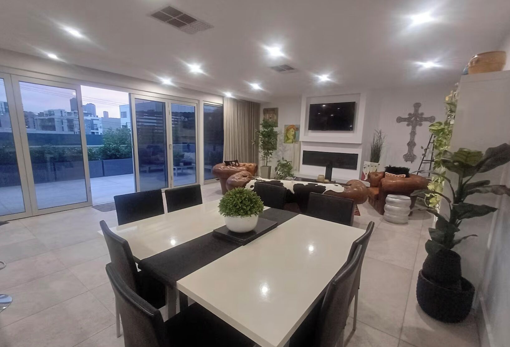 A modern dining area with a large table, chairs, and potted plants.