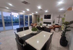 A modern dining area with a large table, chairs, and potted plants. - Luxury 2br CBD View Apartment with spectacular balcony! (Kent Town)