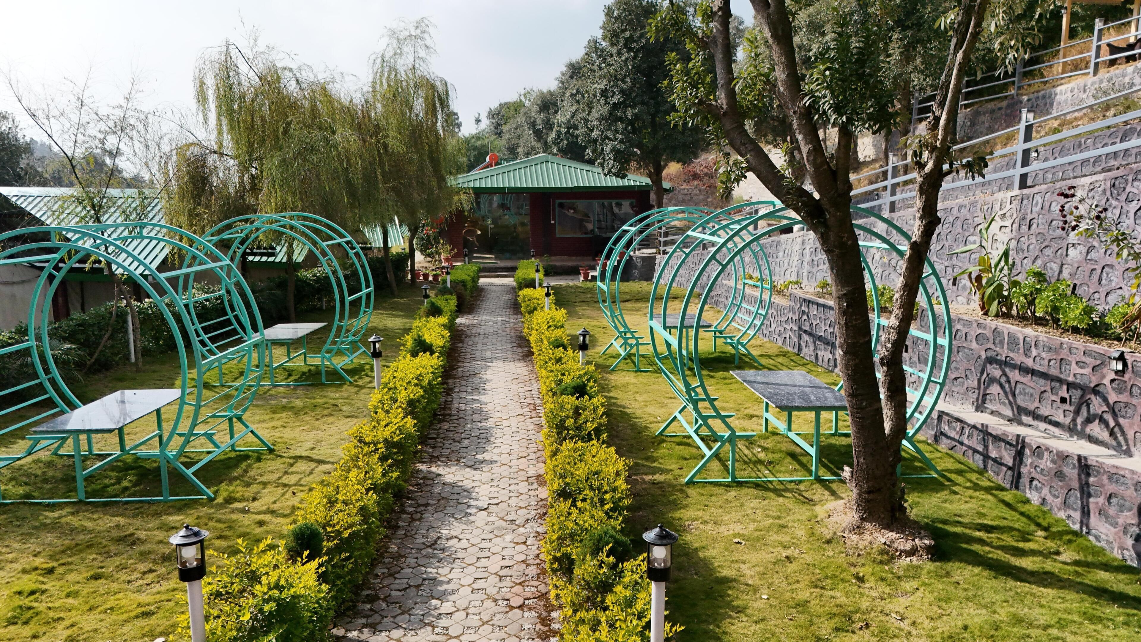 A garden pathway with green metal arches, a gazebo, and stone walls.