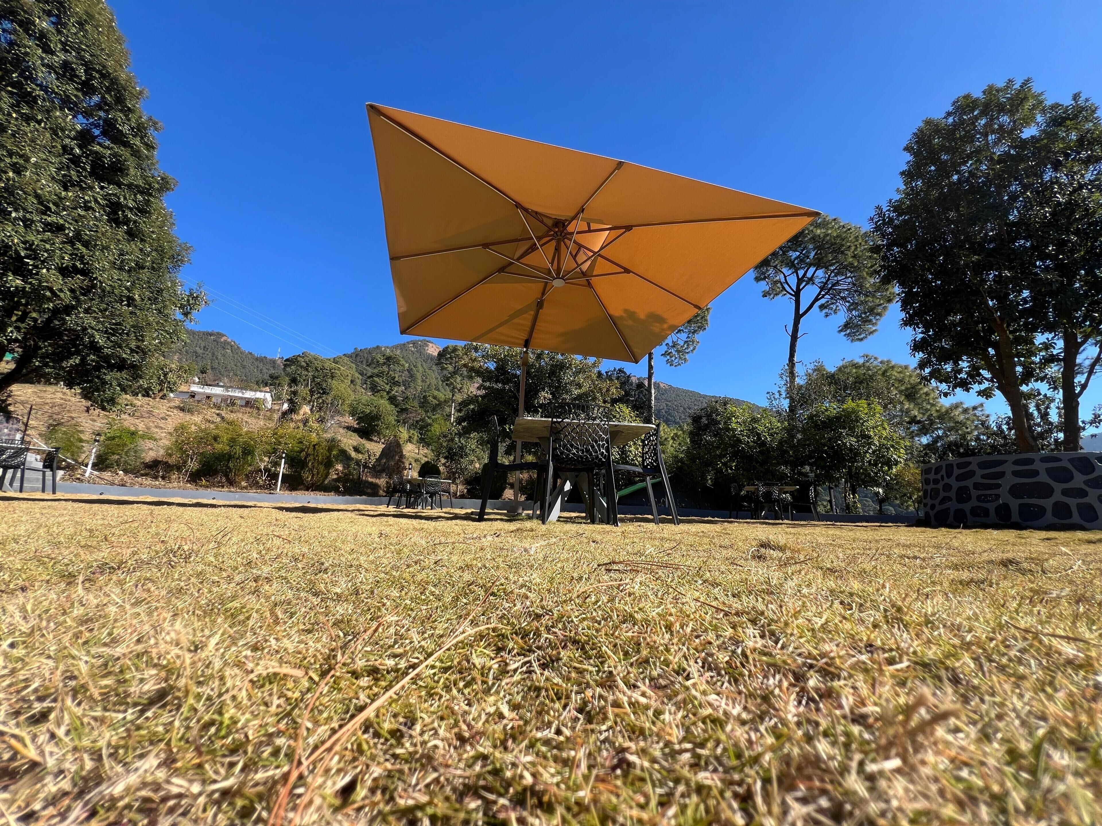 A grassy area with a large yellow umbrella, trees, and a mountain in the background.