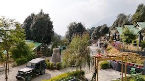 A rural setting with a jeep parked near a stone structure, surrounded by greenery and traditional buildings with green roofs.