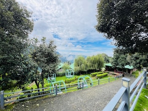 Um caminho que leva a um parque com equipamentos de ginástica, cercado por árvores e vista para montanhas ao longe.