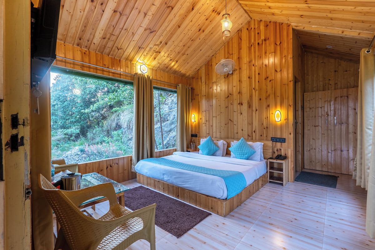Une chambre dans une cabane en bois, avec un lit, des tables de chevet, une chaise et de grandes fenêtres.
