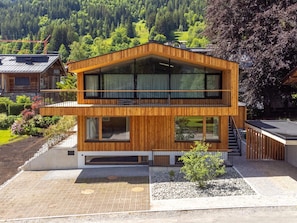 Eine zweistöckige Holzhütte mit großen Fenstern, einem Balkon und Blick auf ein bewaldetes Tal.