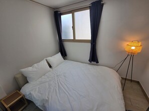 A bedroom with a bed, a nightstand, a window with curtains, and a floor lamp. - Cozy 1-bedroom apartment in tranquil Seoul with AC near Metro Line 2 & 5 (Seoul)