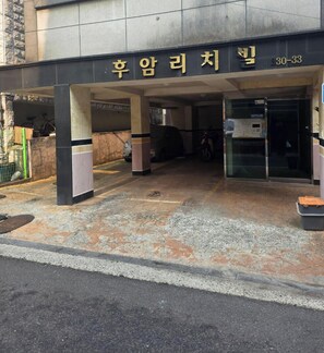 Ein Gebäudeeingang mit einem Schild in Koreanisch, ein überdachter Parkbereich und ein Fahrrad davor.