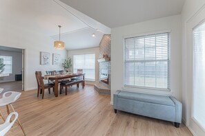 Una habitación amplia con piso de madera, una mesa de comedor con sillas, un banco y una chimenea.