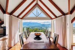 A dining room with a view of mountains, a large wooden table, and curtains. - Mount View Estate - A Luxury Getaway with Unforgettable Views (Yarra Junction)