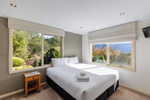 A bedroom with a large bed, two windows, a nightstand, and a TV on the wall. - Mount View Estate - A Luxury Getaway with Unforgettable Views (Yarra Junction)