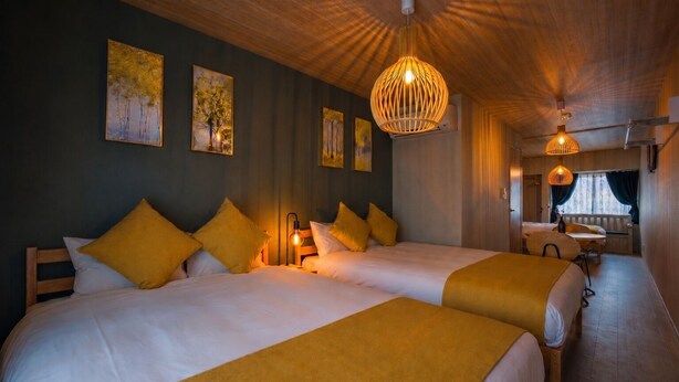 A hotel room with two beds, a small table, and a bench. - Rose House (Osaka Nishinari)
