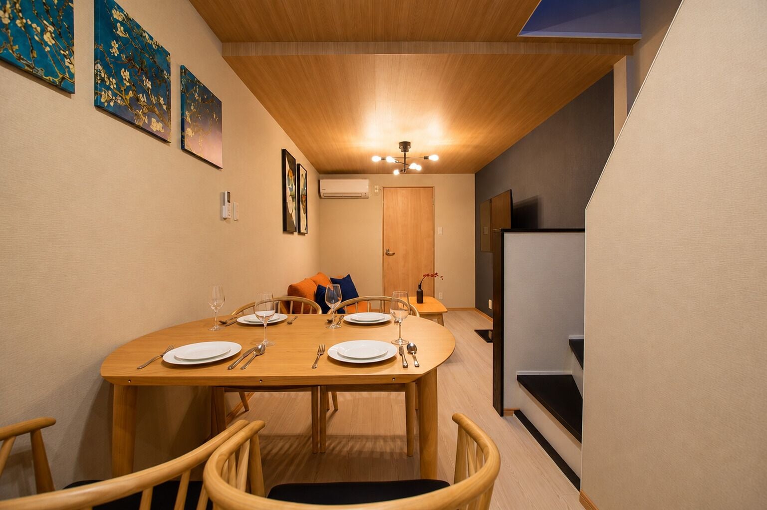 A dining area with a wooden table set for four, chairs, a ceiling light, and artwork on the walls.