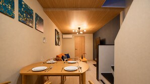 A dining area with a wooden table set for four, chairs, a ceiling light, and artwork on the walls. - Rose House (Osaka Nishinari)