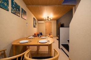 A dining area with a wooden table set for four, chairs, a ceiling light, and artwork on the walls. - Rose House (Osaka Nishinari)