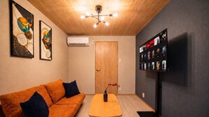 A room with a wooden ceiling, a sofa with cushions, a table with a vase, and a wall-mounted TV displaying movie posters. - Rose House (Osaka Nishinari)