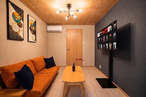 A room with a wooden ceiling, a sofa with cushions, a table with a vase, and a wall-mounted TV displaying movie posters. - Rose House (Osaka Nishinari)