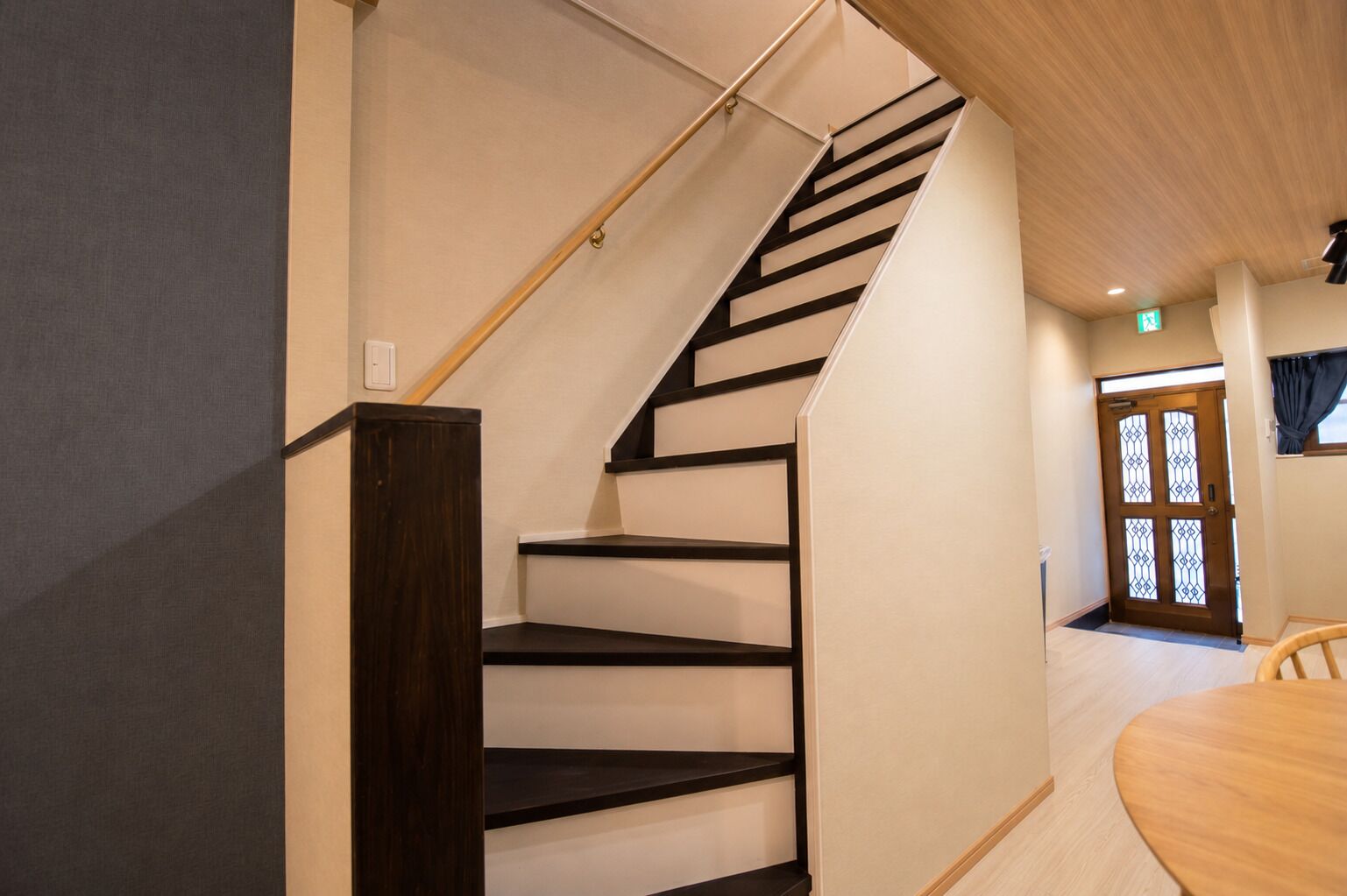 A staircase with a wooden handrail and black steps, leading to a room with a wooden floor and a door with a window.