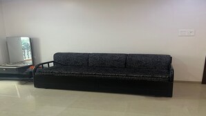 En sort sofa med et mønstret design i et rum med flisegulv og hvid væg.
