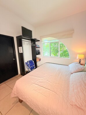 Een slaapkamer met een bed, een kledingkast, een bureau, een stoel en een raam met uitzicht op groen.