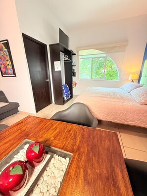 Slaapkamer met een bed, een bureau met appels, een stoel, een garderobe en een raam met uitzicht op groen.