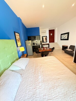 Quarto de hotel com cama, escrivaninha, cozinha compacta e escada para outro andar.