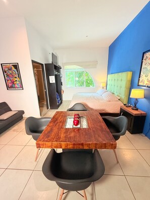Hotelkamer met een bed, een eettafel met appels, een bank, een televisie en uitzicht op groen buiten.
