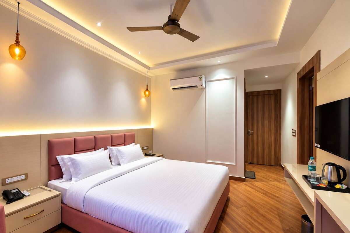 A hotel room with a bed, bedside table, nightstand, wall-mounted TV, ceiling fan, and an air conditioning unit.