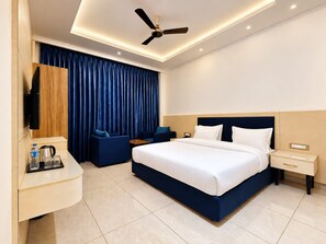 Una habitación de hotel moderna con una cama grande, un escritorio con televisor de pantalla plana, un ventilador de techo y un ventanal con cortinas.