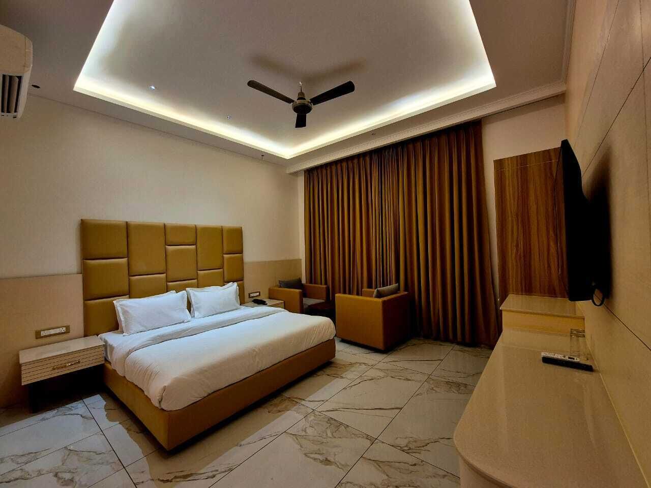 A modern hotel room with a large bed, a ceiling fan, a TV, and a desk.