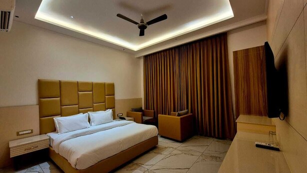 A modern hotel room with a large bed, a ceiling fan, a TV, and a desk. - Hotel Satyaki Orchid (Katra)
