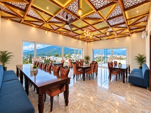A spacious dining area with a long table, multiple chairs, and a ceiling with geometric patterns. - Hotel Satyaki Orchid (Katra)