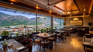 A terrace dining area with tables and chairs, a view of a cityscape and mountains, and a sign reading 'AHELIYA TERRACE DINING'. - Hotel Satyaki Orchid (Katra)