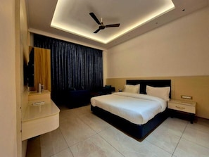 A modern hotel room with a bed, bedside tables, a ceiling fan, and a dark curtain. - Hotel Satyaki Orchid (Katra)