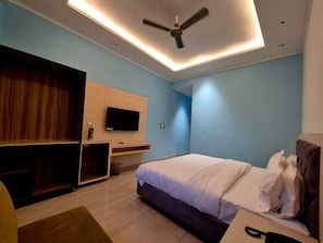 A bedroom with a bed, a TV, a ceiling fan, and a desk. - Hotel Satyaki Orchid (Katra)