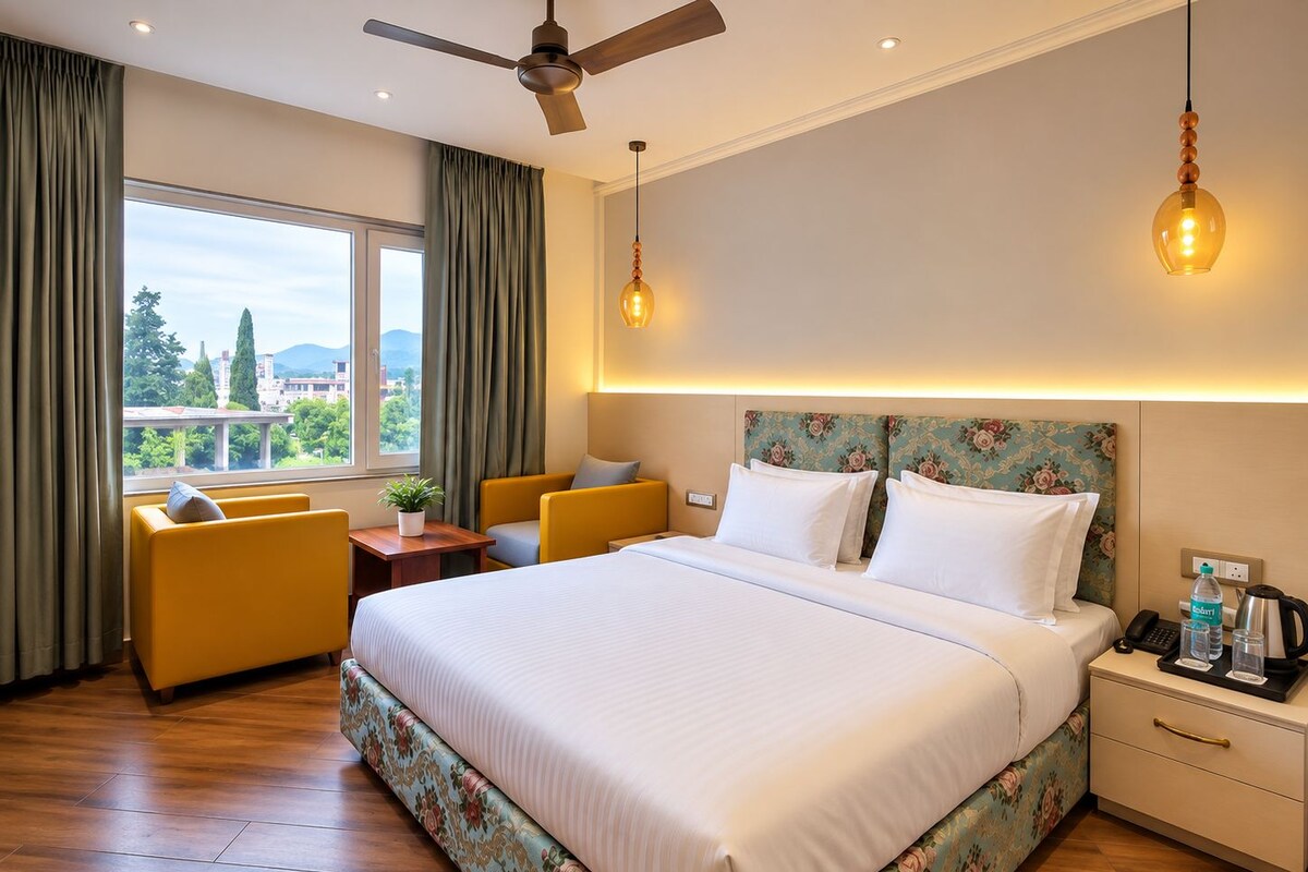 A hotel room with a bed, two yellow armchairs, a nightstand, a ceiling fan, and a view of the outdoors.