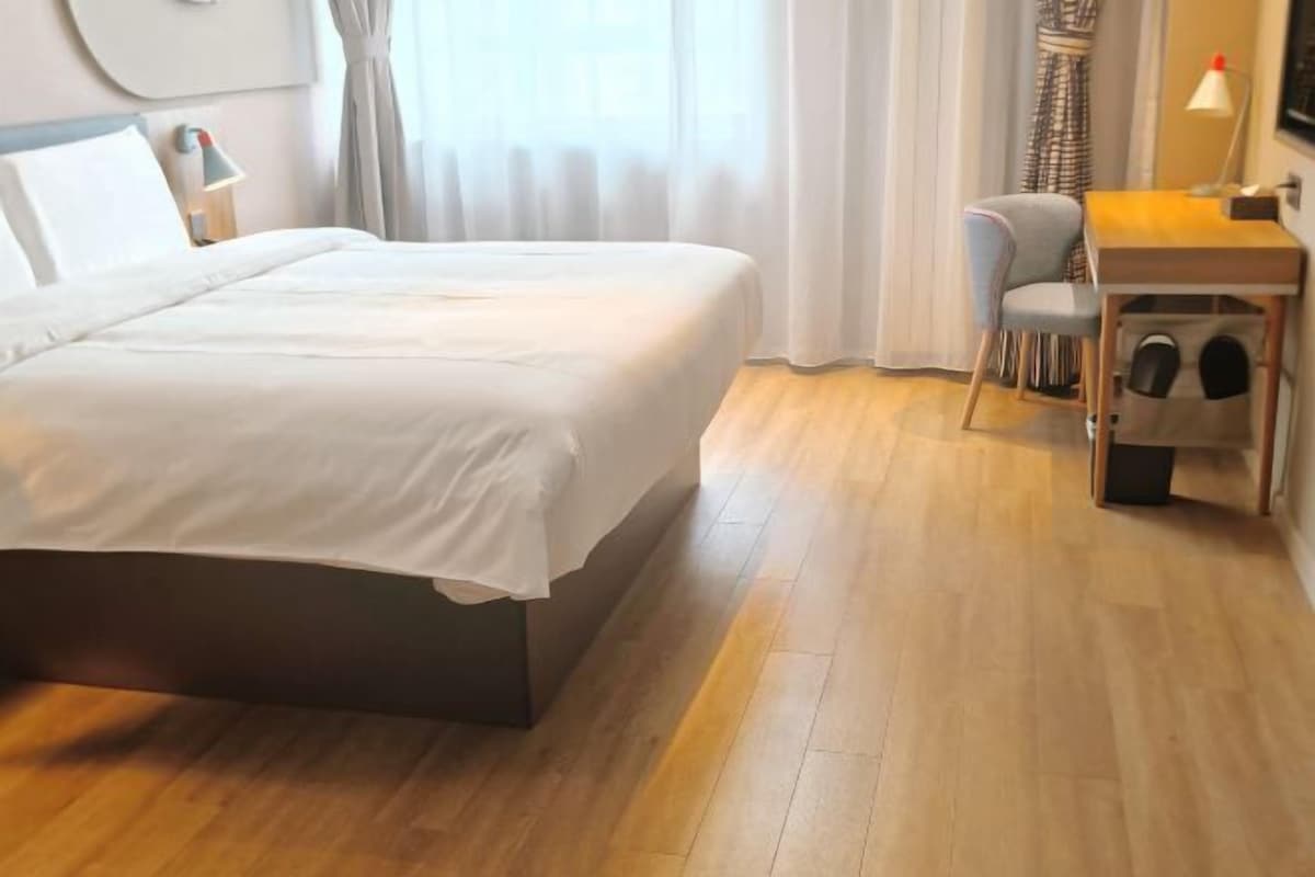 Ein Hotelzimmer mit einem großen Bett, einem Schreibtisch mit Lampe, einem Sessel und einem kleinen Tisch ebenfalls mit Lampe.