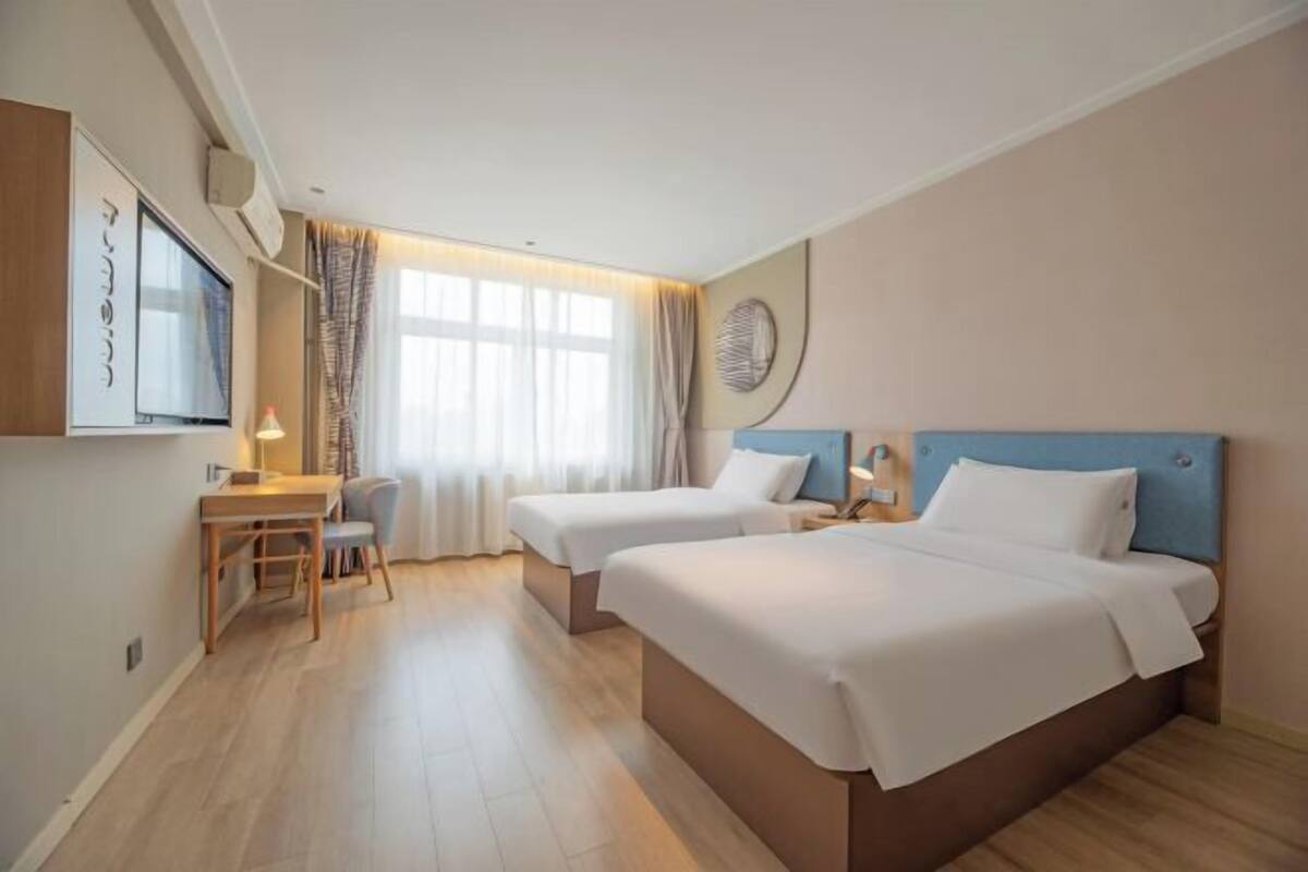 A hotel room with two beds, a desk, and a TV.