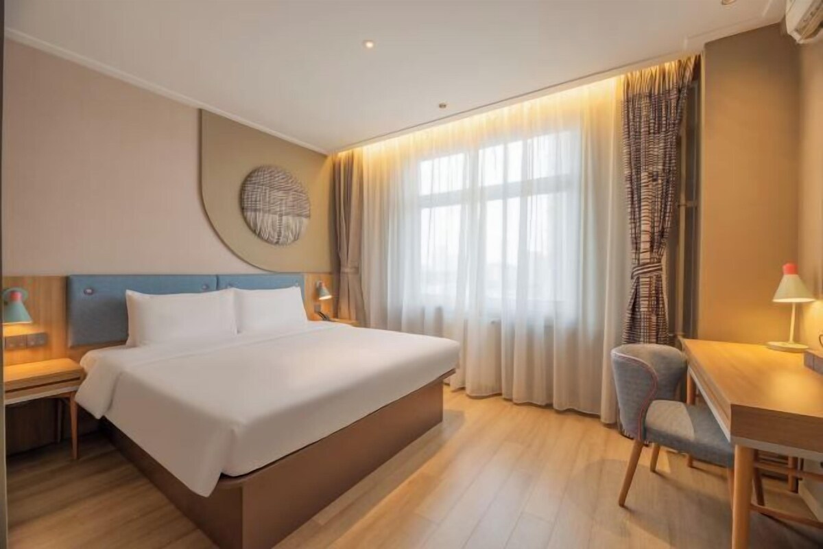 Ein Hotelzimmer mit einem großen Bett, einem Schreibtisch, einem Stuhl, einer runden Wanddekoration und einem Fenster mit Vorhängen.