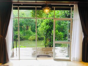 A room with large sliding glass doors leading to an outdoor area with a view of greenery and a water body. - Kithulgala Cabana Resort (Kithulgala)
